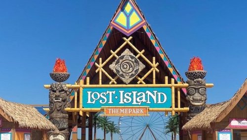 Colorful entrance to Lost Island Themepark, featuring tiki statues and vibrant decorations against a clear blue sky.