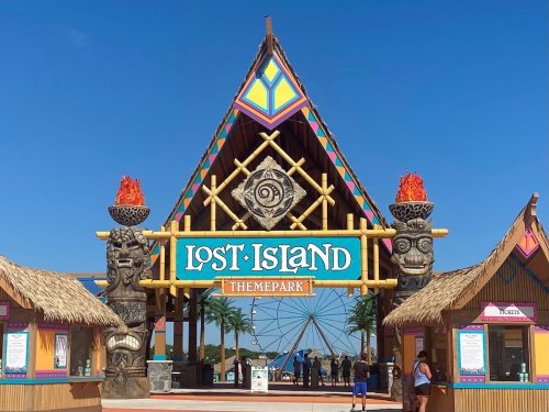 Colorful entrance to Lost Island Theme Park, featuring tiki statues and vibrant decorations against a clear blue sky.