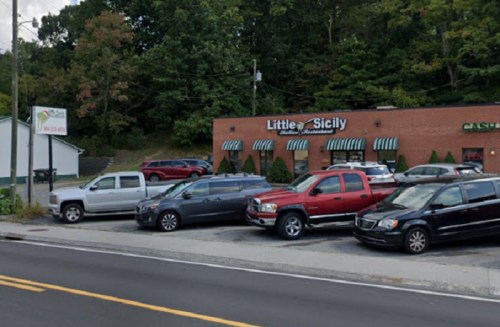 A restaurant named "Little Sicily" with parked cars in front, surrounded by trees and a clear sky.