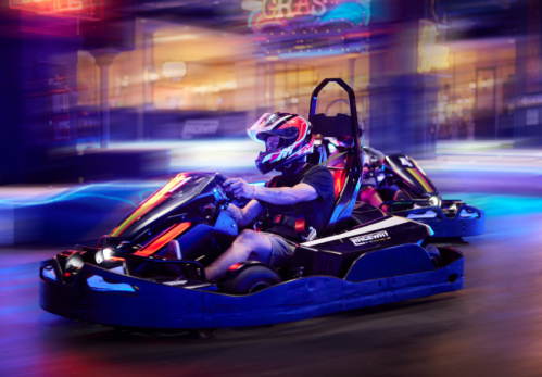 A person in a racing helmet drives a go-kart at night, surrounded by colorful lights and motion blur.