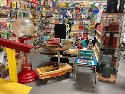 A vintage-themed room filled with retro toys, collectibles, and colorful lunchboxes, featuring a gumball machine and Mickey Mouse decor.