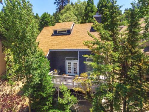 A cozy house with a sloped roof surrounded by tall trees and a deck, set in a lush green landscape.