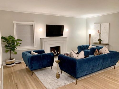 A cozy living room featuring blue sofas, a TV above a fireplace, a plant, and modern decor on light walls.