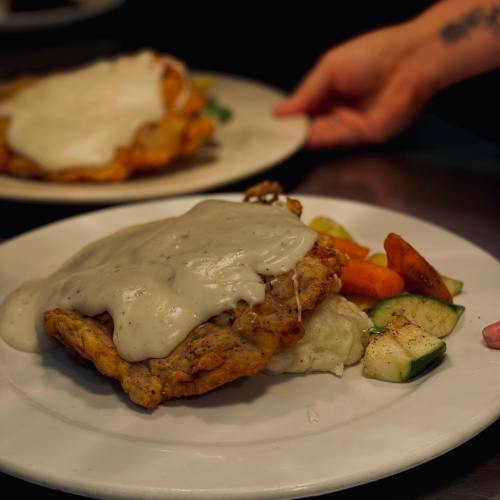A plate of fried chicken smothered in gravy, served with mixed vegetables and mashed potatoes.
