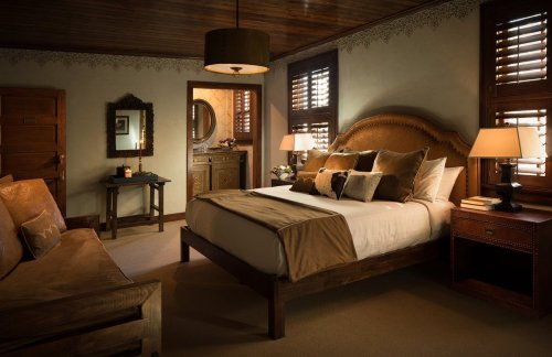 Cozy bedroom with a large bed, decorative pillows, wooden furniture, and soft lighting, featuring a warm, inviting atmosphere.