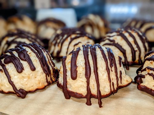 A close-up of coconut macaroons drizzled with chocolate, arranged on a wooden surface.