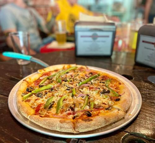 A freshly baked pizza topped with green peppers, onions, and olives, served on a metal tray in a casual dining setting.