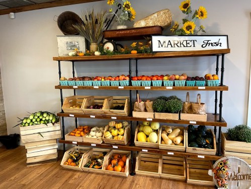 A wooden market display with fresh fruits and vegetables in baskets, surrounded by decorative sunflowers and rustic decor.