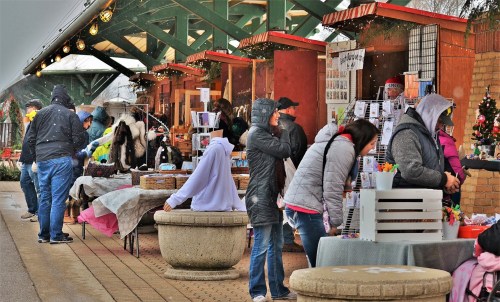 A bustling outdoor market with vendors and shoppers, featuring various stalls and festive decorations.