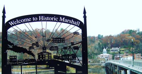 Sign reading "Welcome to Historic Marshall" with a scenic view of the town and bridge in the background.