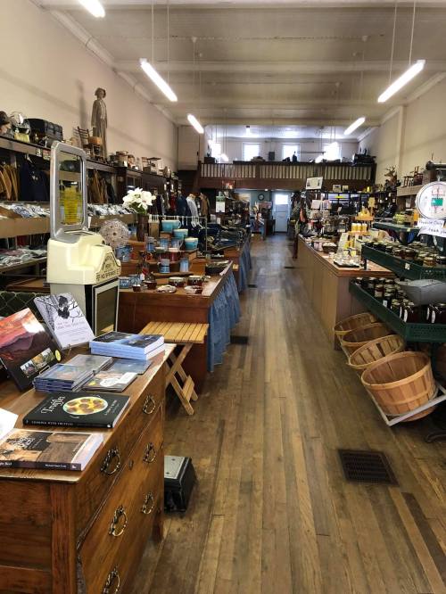 A wide view of a vintage store filled with various kitchenware, wooden furniture, and home goods along a wooden floor.