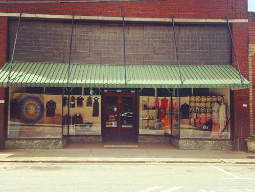 A storefront with a green awning, displaying clothing and accessories in the windows.