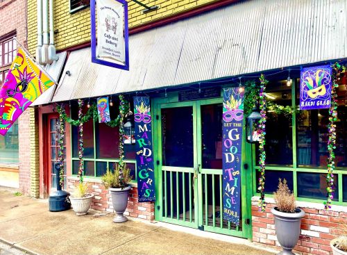 Colorful storefront decorated for Mardi Gras with masks, beads, and festive signs inviting good times.