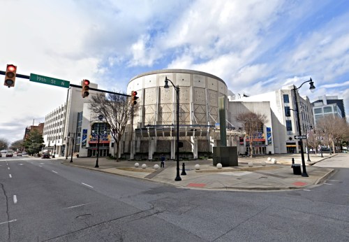 A modern building with a circular design, located at an intersection with traffic lights and trees nearby.