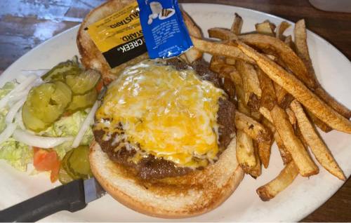 A plate with a cheeseburger topped with melted cheese, fries, and a side of salad and pickles.