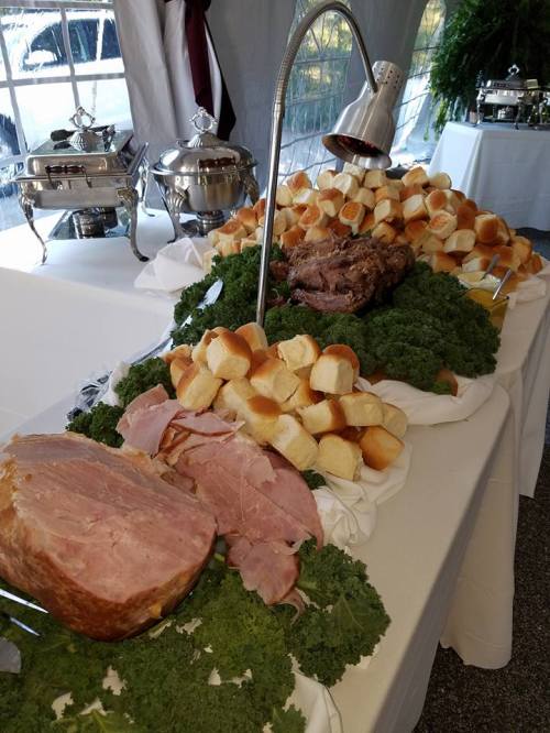A buffet table featuring various meats, rolls, and garnished with kale.