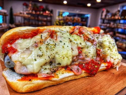 A close-up of a cheesy meat sandwich on a wooden board, topped with marinara sauce and herbs, with a cozy background.