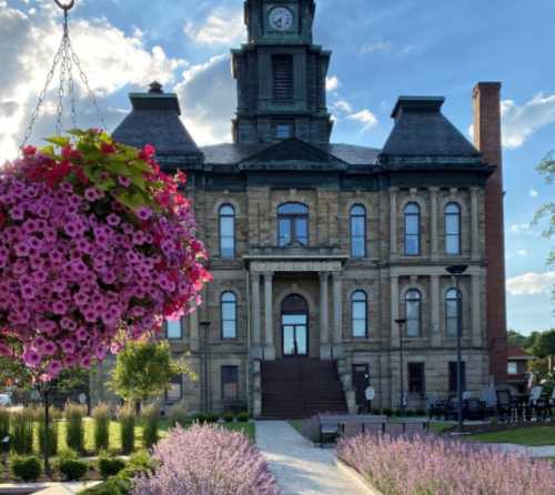 Historic building with a clock tower, surrounded by vibrant flowers and greenery under a blue sky.