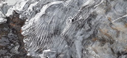 Close-up of textured ice with intricate patterns and a mix of dark and light colors, resembling natural formations.