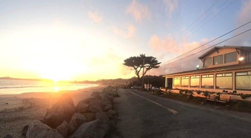 A scenic beach view at sunset, featuring a restaurant by the shore and rocky landscaping along the road.