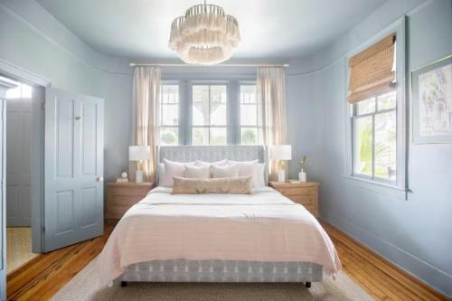 Bright bedroom with blue walls, a large bed, wooden floors, and stylish decor, featuring a chandelier and natural light.