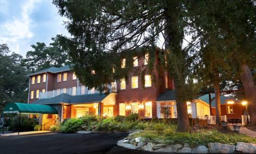 A charming brick hotel surrounded by trees, with warm lights glowing from its windows in the evening.