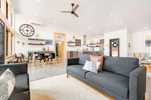 Modern living room with gray sofas, a large clock, and an open kitchen area featuring wooden accents and stylish decor.