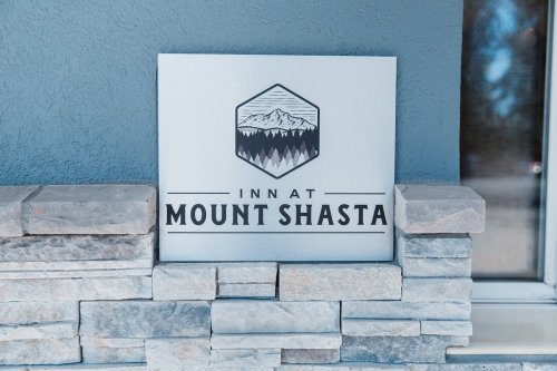 Sign for "Inn at Mount Shasta" featuring a mountain graphic, set against a stone wall.
