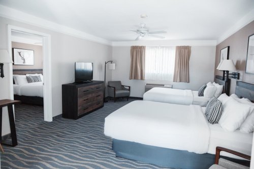 A spacious hotel room with two beds, a TV, and a seating area, featuring neutral decor and natural light.