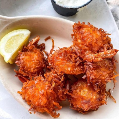 A plate of crispy fried shrimp with a lemon wedge and a small cup of dipping sauce.