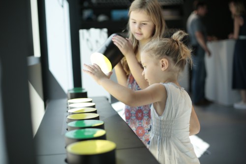 Two young girls interact with colorful light displays in a modern, bright environment.