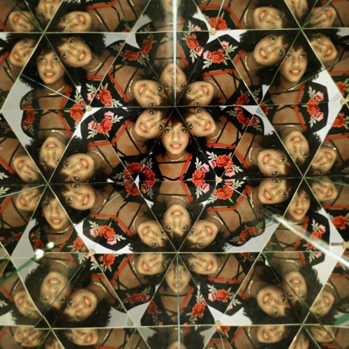 A kaleidoscopic pattern featuring multiple reflections of a woman with curly hair, wearing a floral outfit.