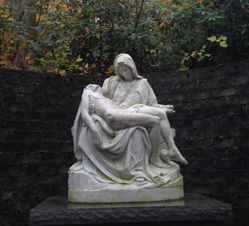 A marble statue of a seated Mary holding the lifeless body of Jesus, set against a stone wall and greenery.