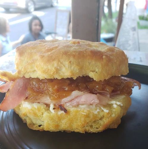 A flaky biscuit sandwich filled with ham and sweet onion jam, served on a plate with a blurred background.