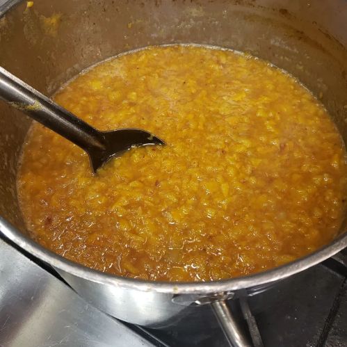 A pot of thick, brown lentil soup with a ladle resting inside, simmering on a stove.