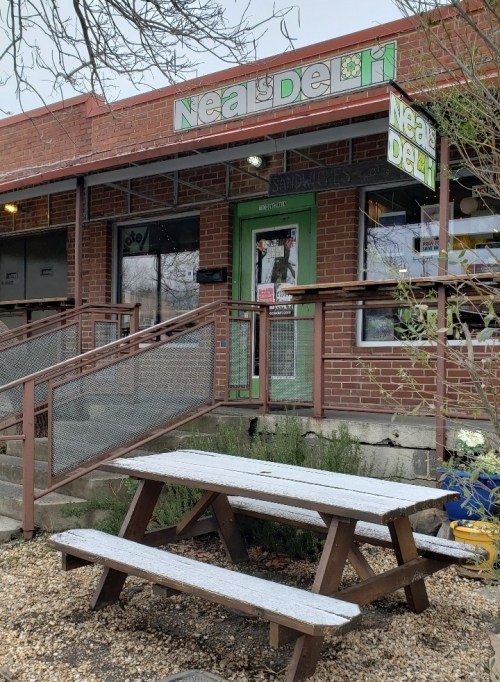 Exterior of Neal's Deli, featuring a green door, sign, and a picnic table in front on a gravel area.
