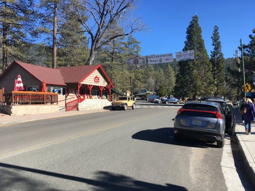 A quaint roadside scene featuring a red building, parked cars, and trees under a clear blue sky.