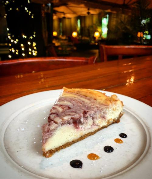 A slice of marbled cheesecake on a white plate, garnished with colorful sauces, set on a wooden table.