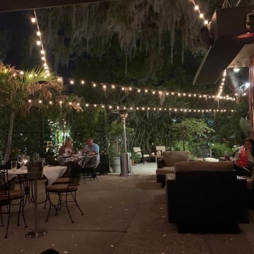 Cozy outdoor dining area with string lights, plants, and guests enjoying a meal in a relaxed atmosphere.