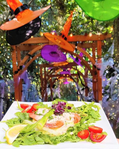 A festive dish of shrimp on a bed of greens, garnished with tomatoes and lemon, with Halloween decorations in the background.