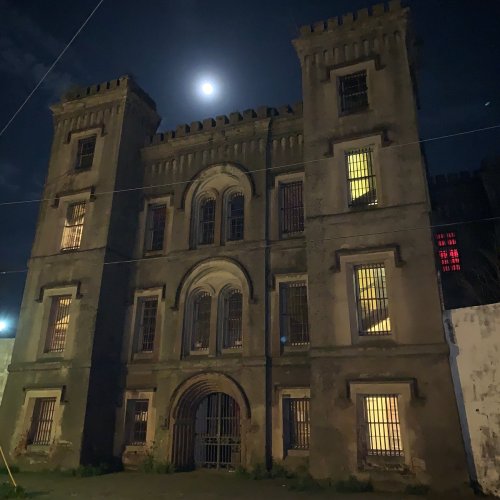 A historic stone building with barred windows, illuminated by moonlight, set against a dark night sky.