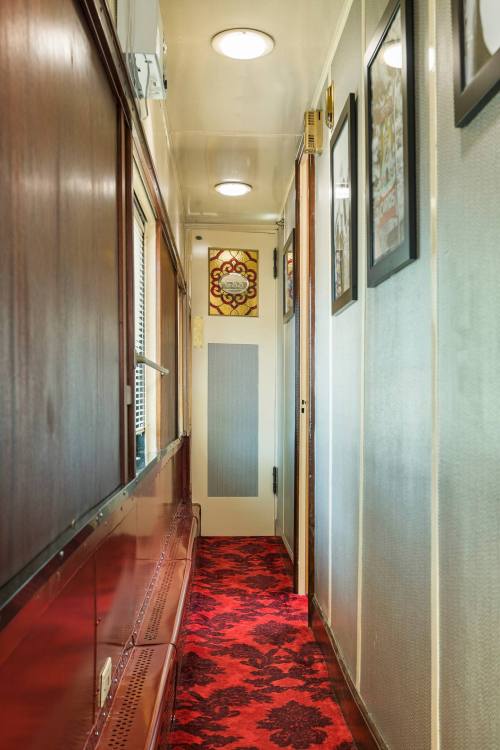 A narrow hallway with wooden paneling, red carpet, and framed artwork on the walls.
