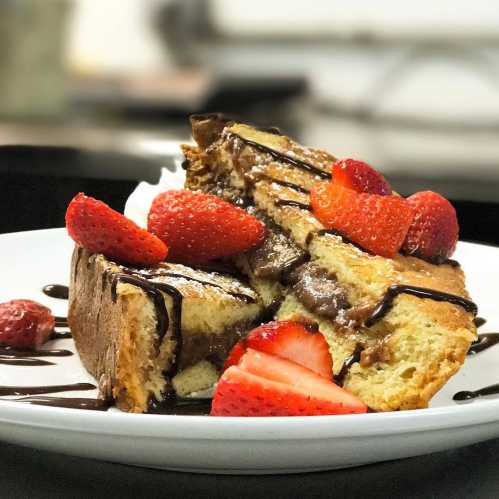 A slice of fluffy cake topped with fresh strawberries and drizzled with chocolate sauce on a white plate.