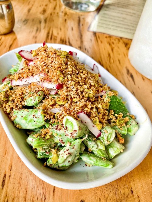 A fresh salad with greens, radishes, and a crunchy topping, served in a white dish on a wooden table.