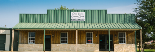 Exterior of Olde Towne Country Store, featuring a green metal roof and wooden facade, under a clear blue sky.