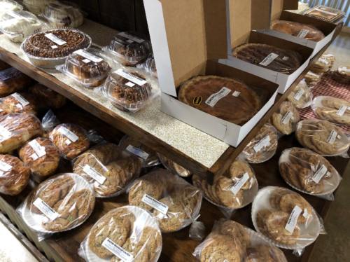 A display of various baked goods, including pies and cookies, arranged on a wooden table with labels.