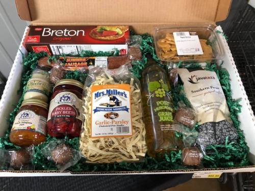 A gift box filled with snacks, including crackers, sausage, noodles, pickled beets, grape juice, and chocolate treats.