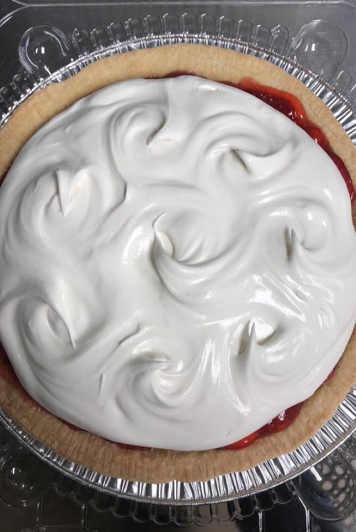 A freshly made pie with a golden crust topped with swirls of whipped cream and a red fruit filling.