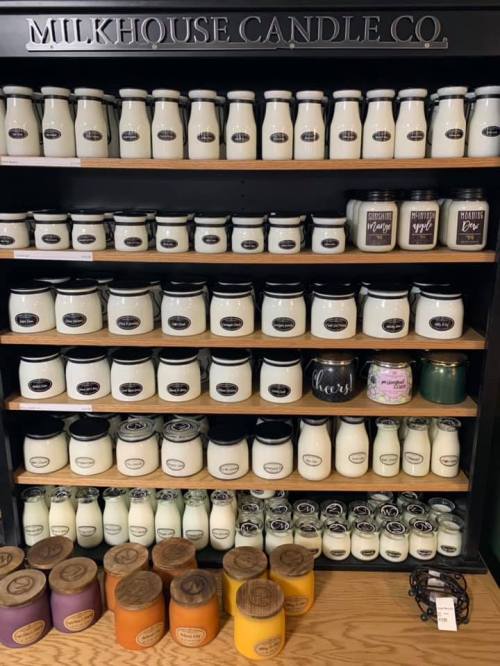 A display of various candles on shelves, labeled with different scents, from Milkhouse Candle Co.