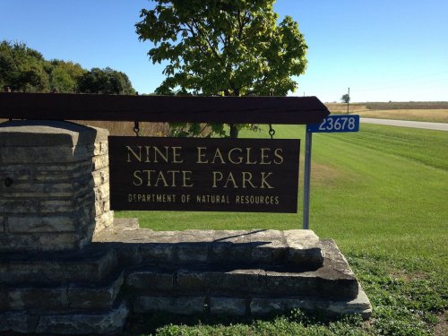 Sign for Nine Eagles State Park, featuring natural scenery and a clear blue sky in the background.